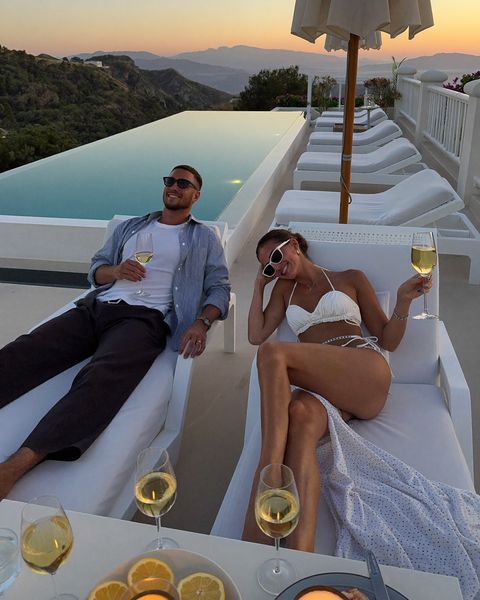 Paar mit Sekt auf einer Terrasse mit Pool bei Sonnenuntergang