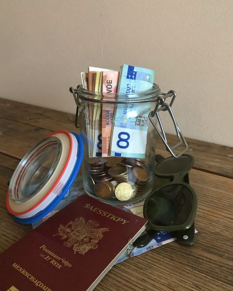 Glas mit Münzen und Scheinen neben Reisepass, Karte und Sonnenbrille