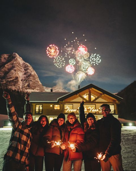 Freunde mit Wunderkerzen vor einer verschneiten Hütte an Silvester